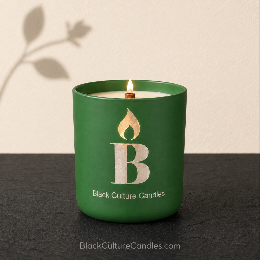 A green glass jar candle with a lit wick sits on a dark surface against a light beige wall. The jar has a large etched letter B and a leaf flame icon, with the text 'Black Culture Candles' printed below.