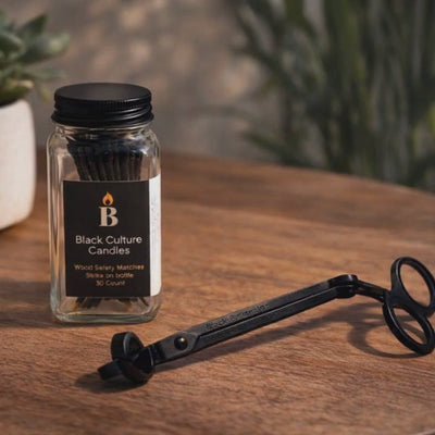 Black Culture Candles candle accessory set with wood safety matches in a glass jar and black metal wick trimmer on a wooden table.